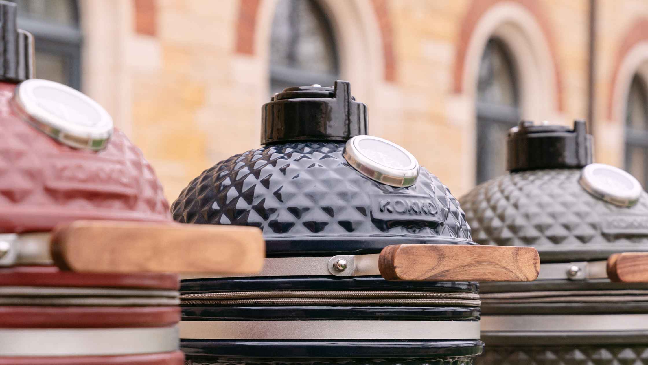 Trois kamados de différentes couleurs posés côte à côte, comparatif de barbecues en céramique polyvalents pour cuisson extérieure