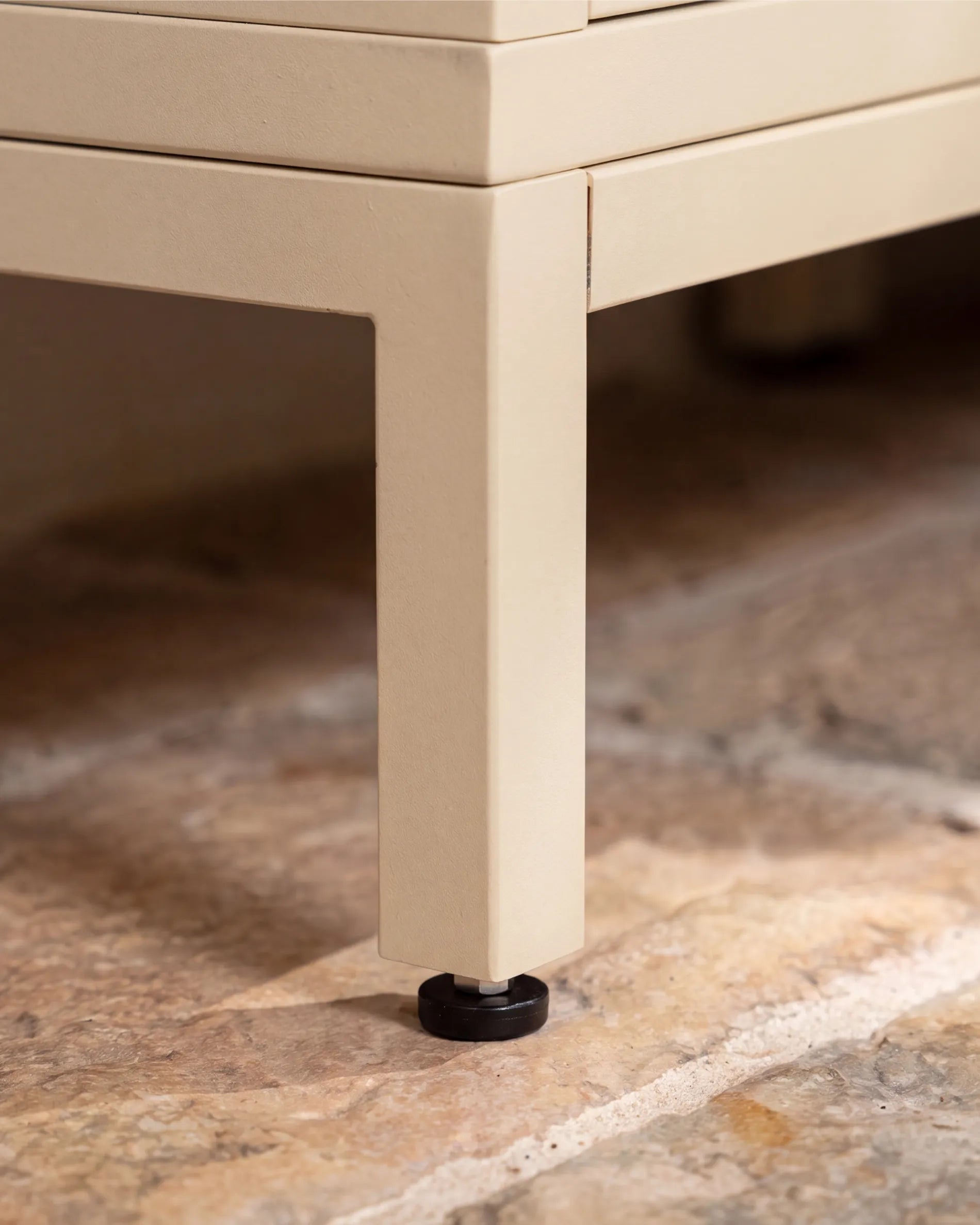 Pied métallique beige crème de la structure PILOTIS avec vérin de nivellement, gros plan sur sol en pierre