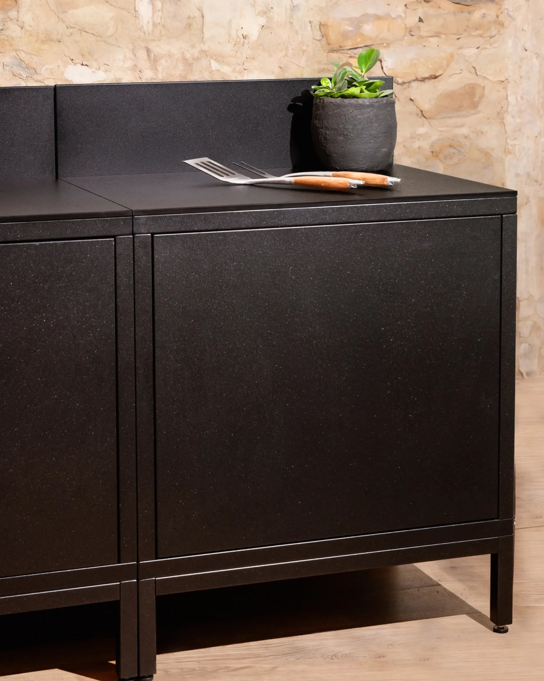 Caisson noir module Classic PILOTIS en cuisine extérieure, plan de travail avec plante et couverts