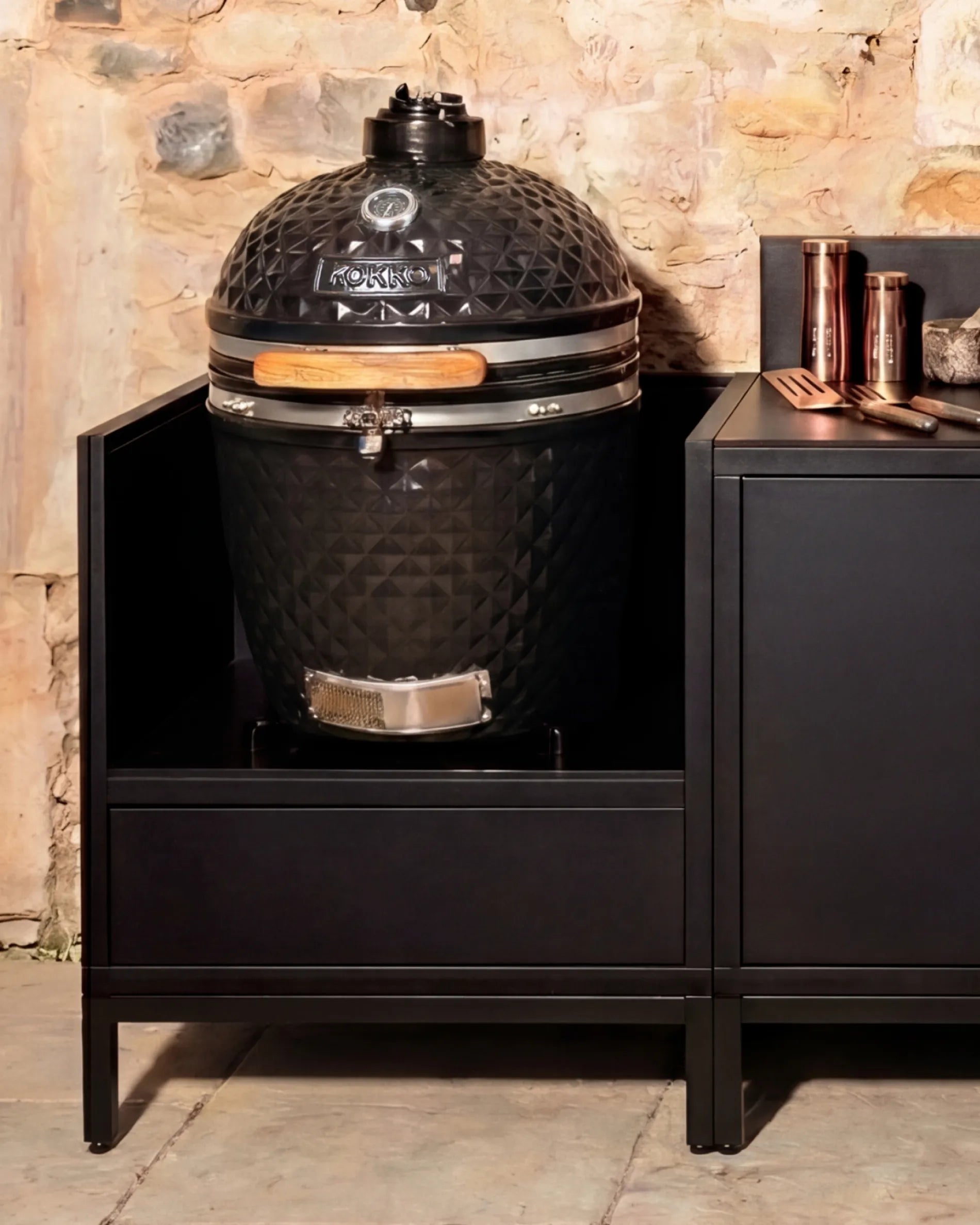 Barbecue kamado noir Kokko installé dans caisson PILOTIS avec accessoires en cuivre, cuisine extérieure